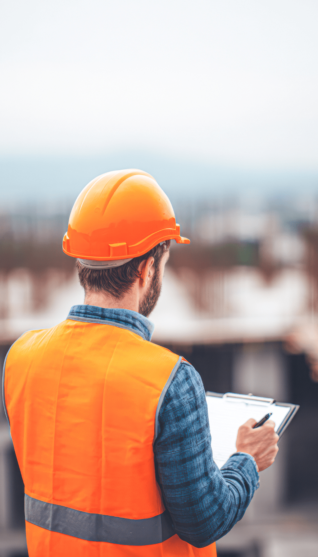 Construction Safety Inspection on Site Construction site inspector wearing orange safety vest and hard hat reviewing checklist during site inspection.