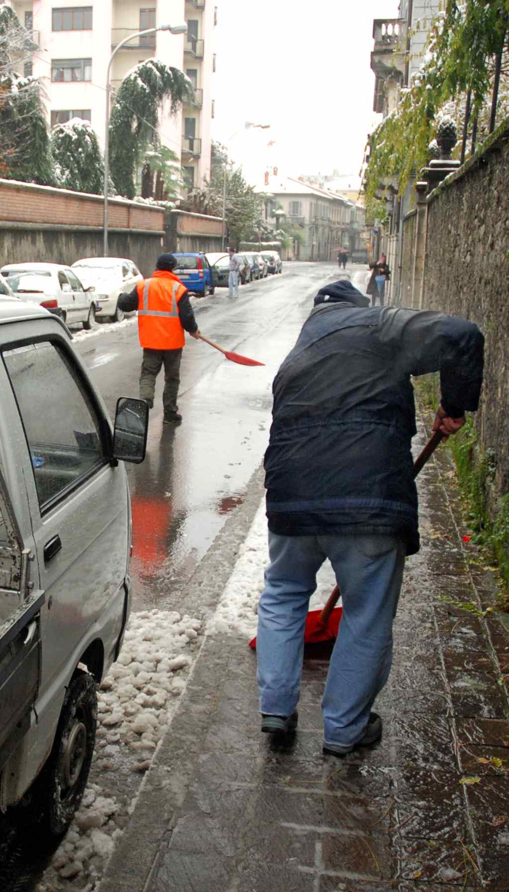 Road Workers Clearing Snow During a Winter Storm — Safety on the Job Two road workers wearing high-visibility jackets clearing snow during a heavy winter storm with a snowplow in the background