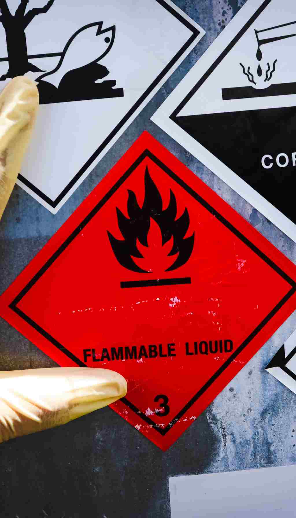 Flammable Liquid Hazard Labels in Chemical Safety Compliance Close-up of flammable liquid hazard label and other chemical warning symbols, with a gloved hand applying the label as part of chemical safety and CLP compliance.