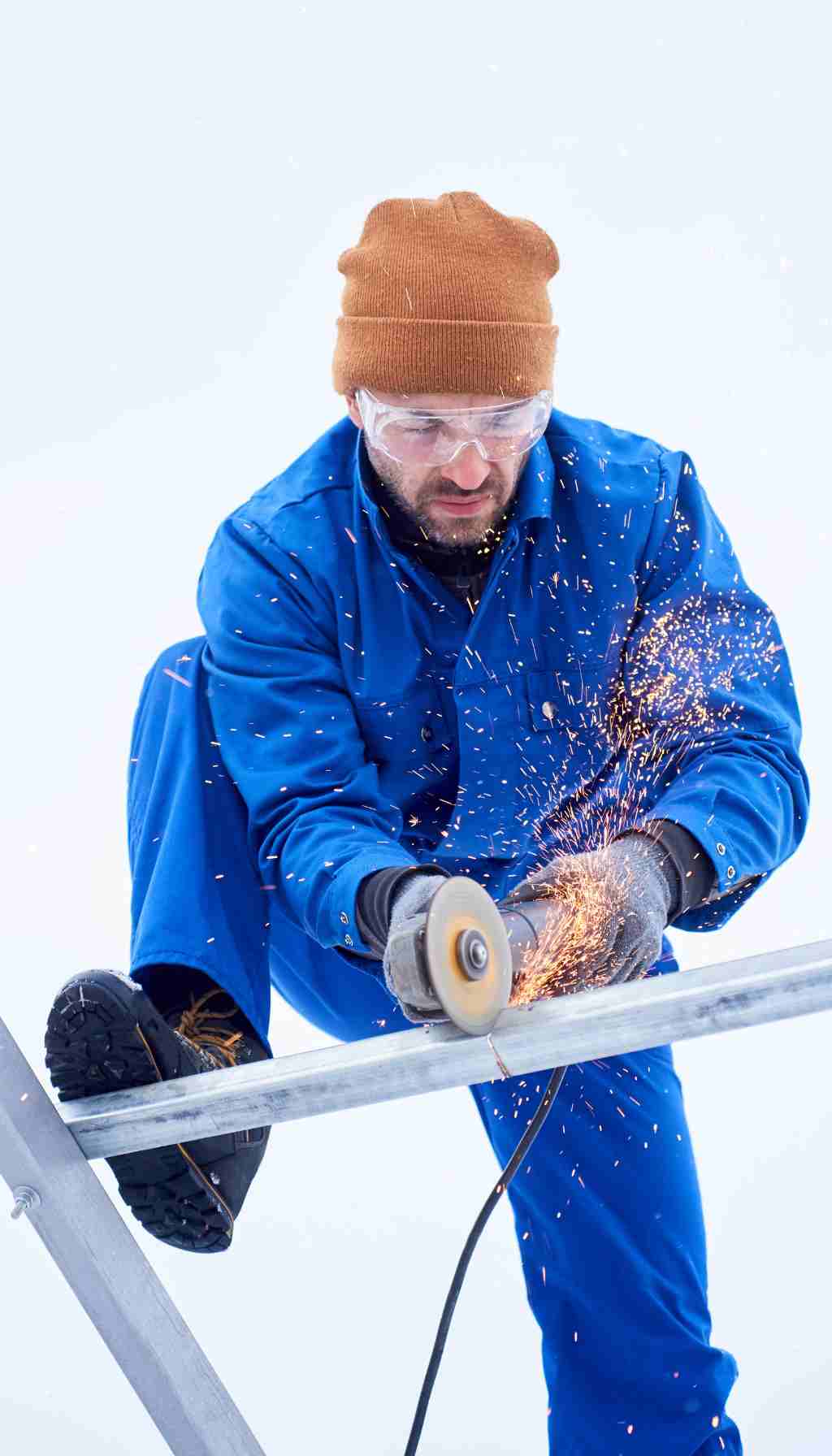 Outdoor Winter Work Safety: Grinding Metal in Cold Conditions Worker using an angle grinder on a metal bar outdoors in snowy winter conditions, wearing protective eyewear and warm clothing.