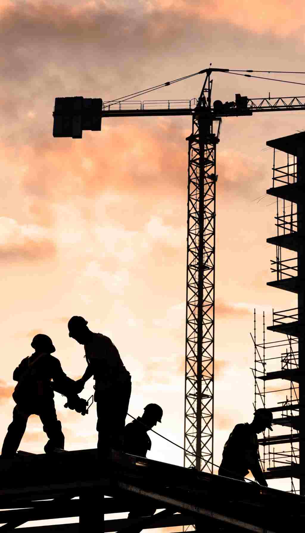 Construction Site Safety – Protecting Workers at Height Silhouetted construction workers on a building site with cranes at sunset, demonstrating safe work practices