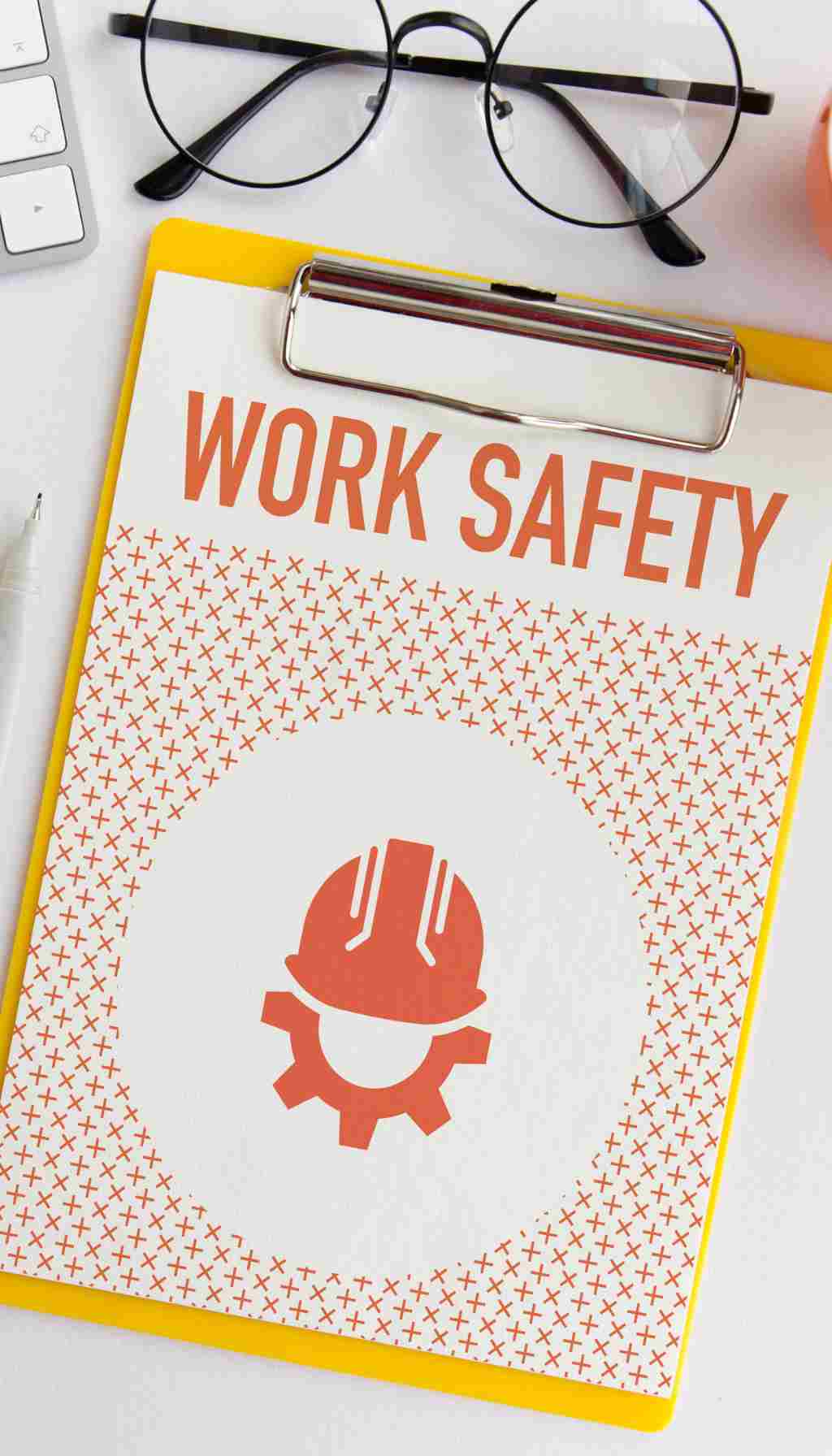 Workplace Safety Checklist – Health and Safety Compliance Clipboard with “Work Safety” heading and hard hat icon, placed on a desk with glasses and office items