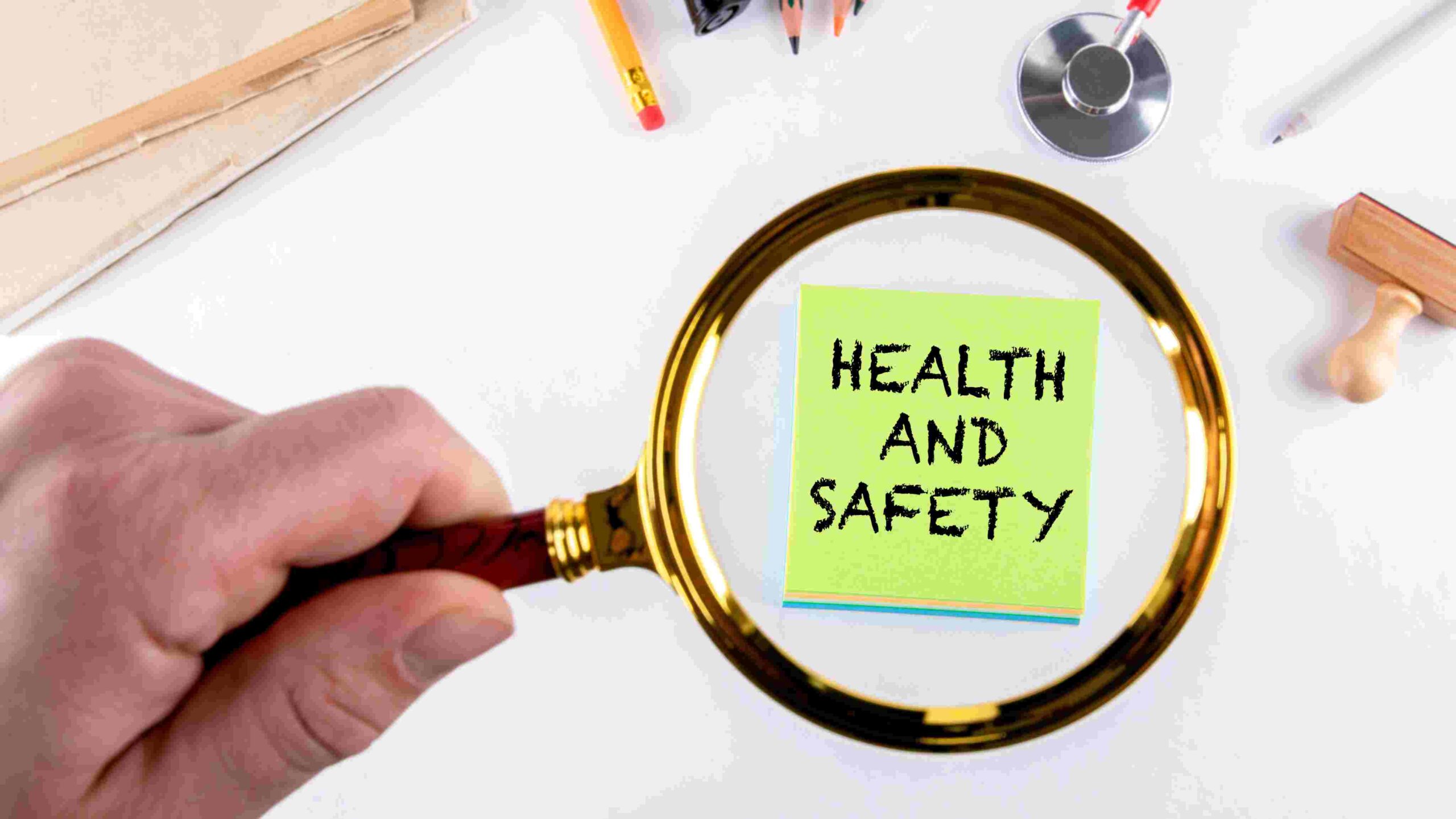 Health and Safety Focus – Workplace Compliance and Risk Management Magnifying glass highlighting a note that says “Health and Safety” on a desk with work items