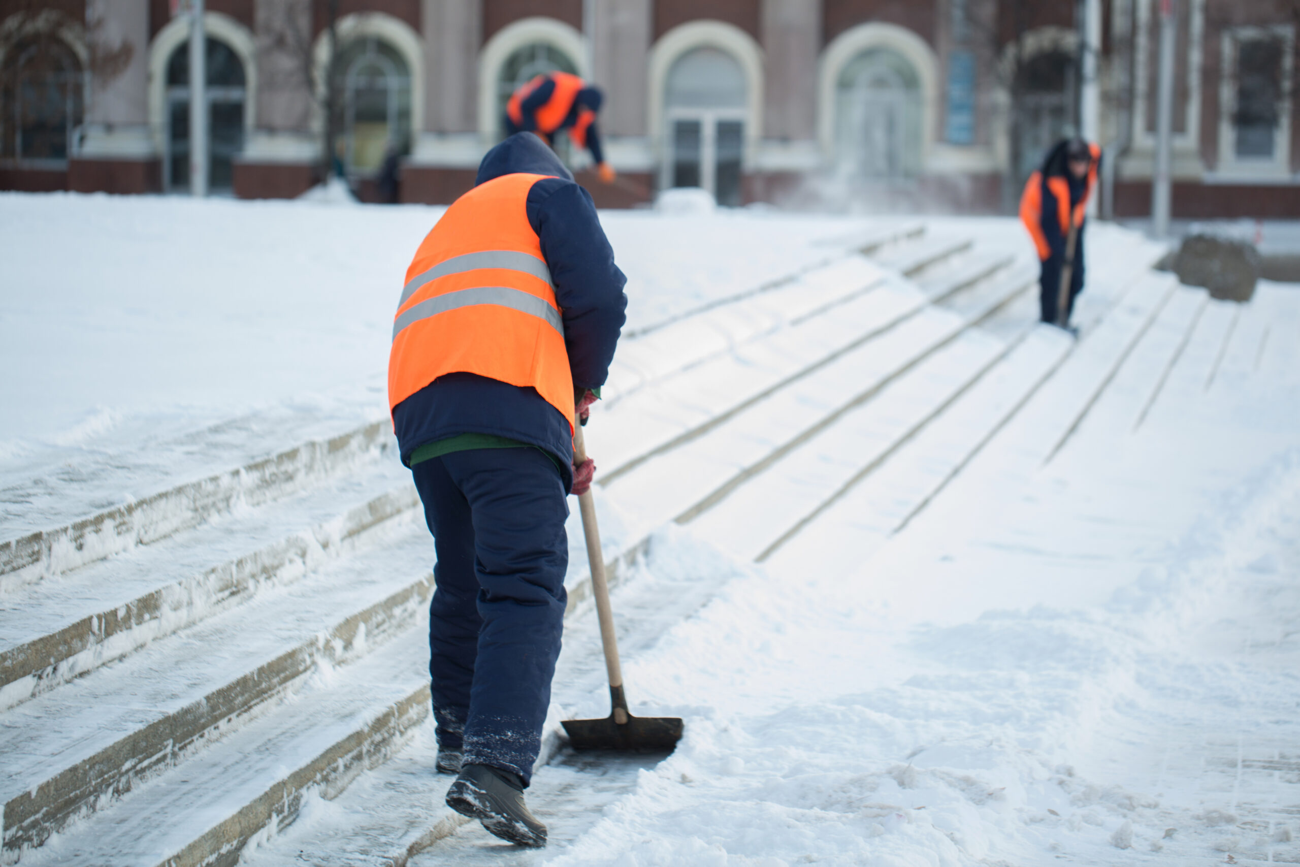 Winter Snow Clearing on Outdoor Steps for Workplace Safety Workers in high-visibility vests shovelling snow from outdoor steps in icy winter conditions.