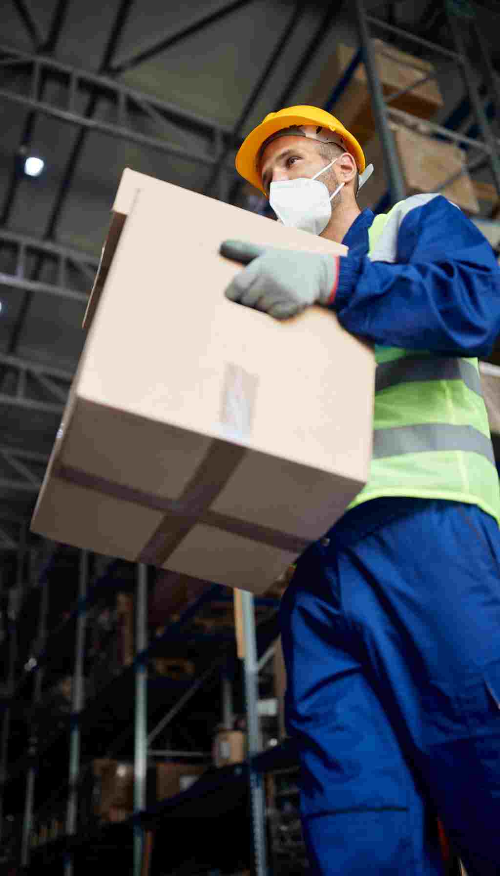 Warehouse worker wearing PPE and lifting a cardboard box safely to illustrate proper manual handling techniques and injury prevention.