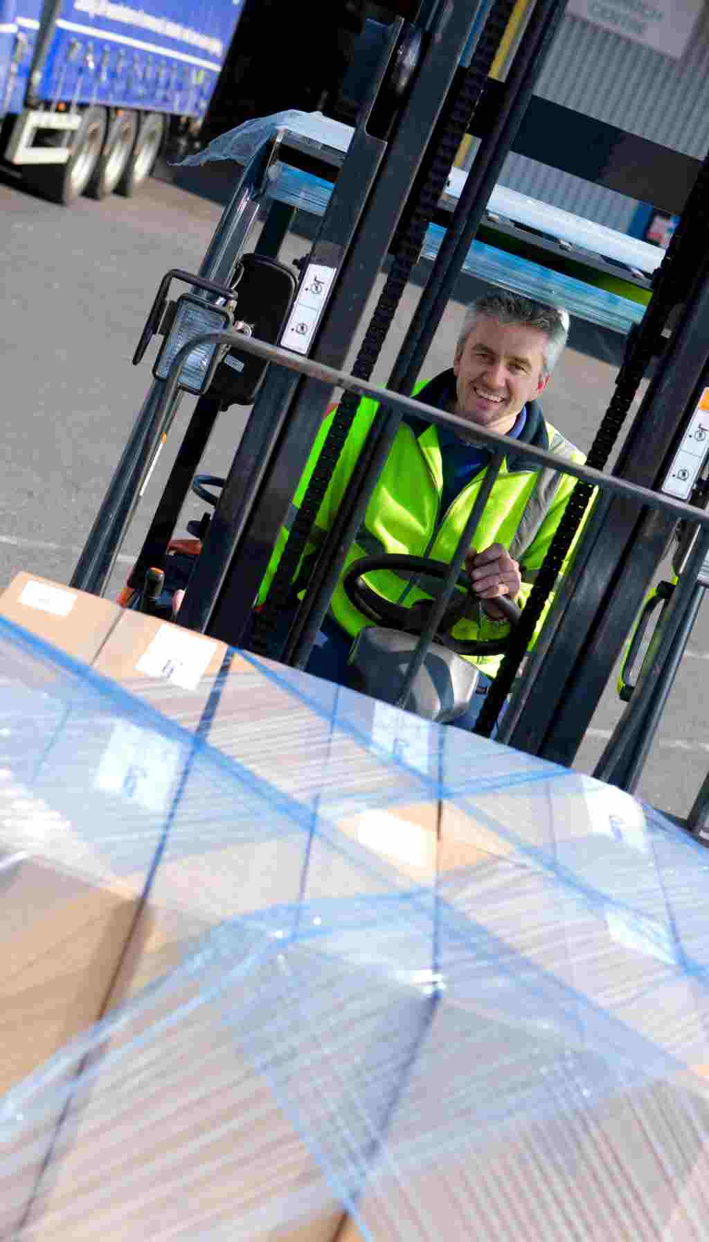 Warehouse worker driving a forklift to move a wrapped pallet safely, demonstrating mechanical handling as an alternative to manual lifting.