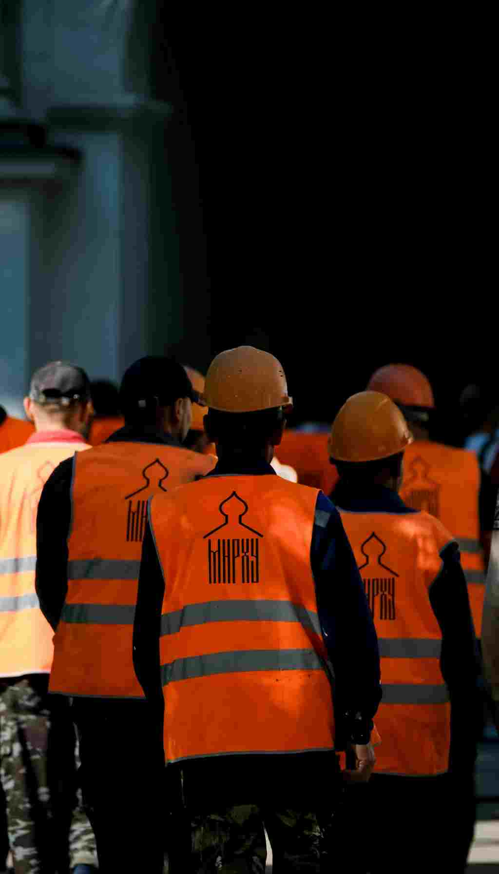 Construction Workers Wearing High-Visibility PPE on Site Group of construction workers wearing orange high-visibility vests and hard hats while walking on a worksite.