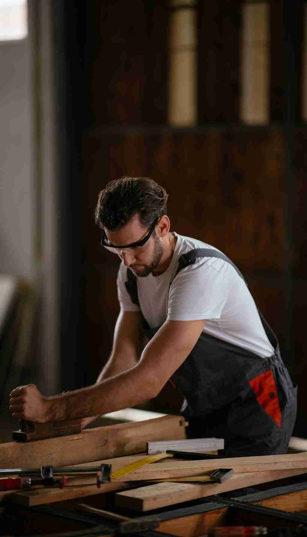 Carpenter Using Hand Tools Safely in the Workshop Worker wearing safety glasses while using a hand tool to plane wood in a workshop.