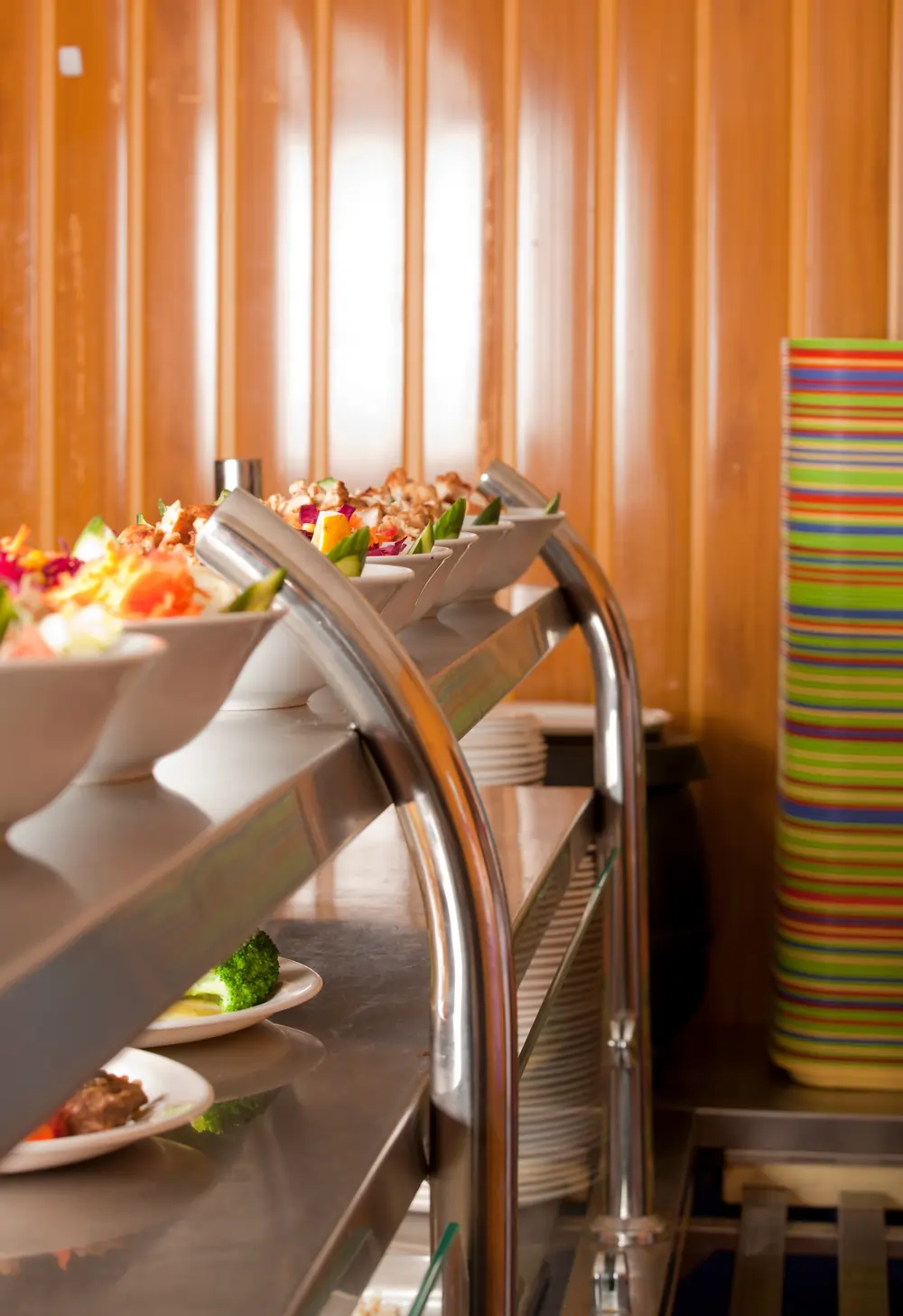 Prepared plates of food displayed on a stainless-steel canteen service counter, showing salads and hot meal components ready for service in an Irish catering or school kitchen.