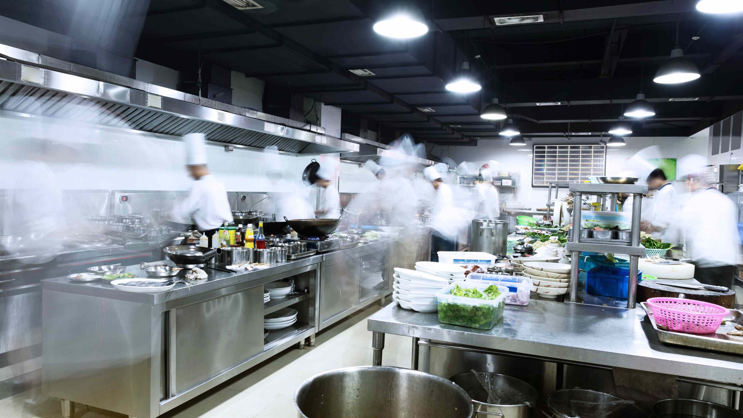 Busy commercial kitchen with chefs working quickly at multiple stations, illustrating a high-activity food preparation environment.