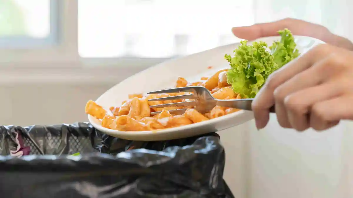 Employee disposing of leftover catered food in an office kitchen bin, illustrating food hygiene practices and employer responsibility for workplace safety in Ireland.