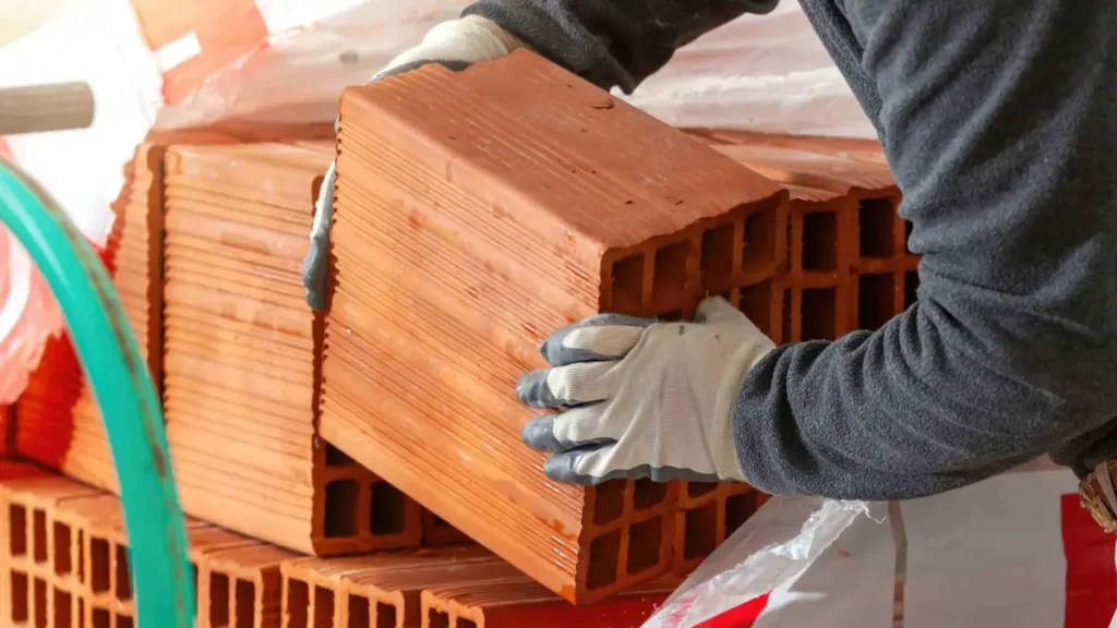Worker wearing protective gloves lifting a heavy construction block, demonstrating the risks of improper manual handling on building sites.