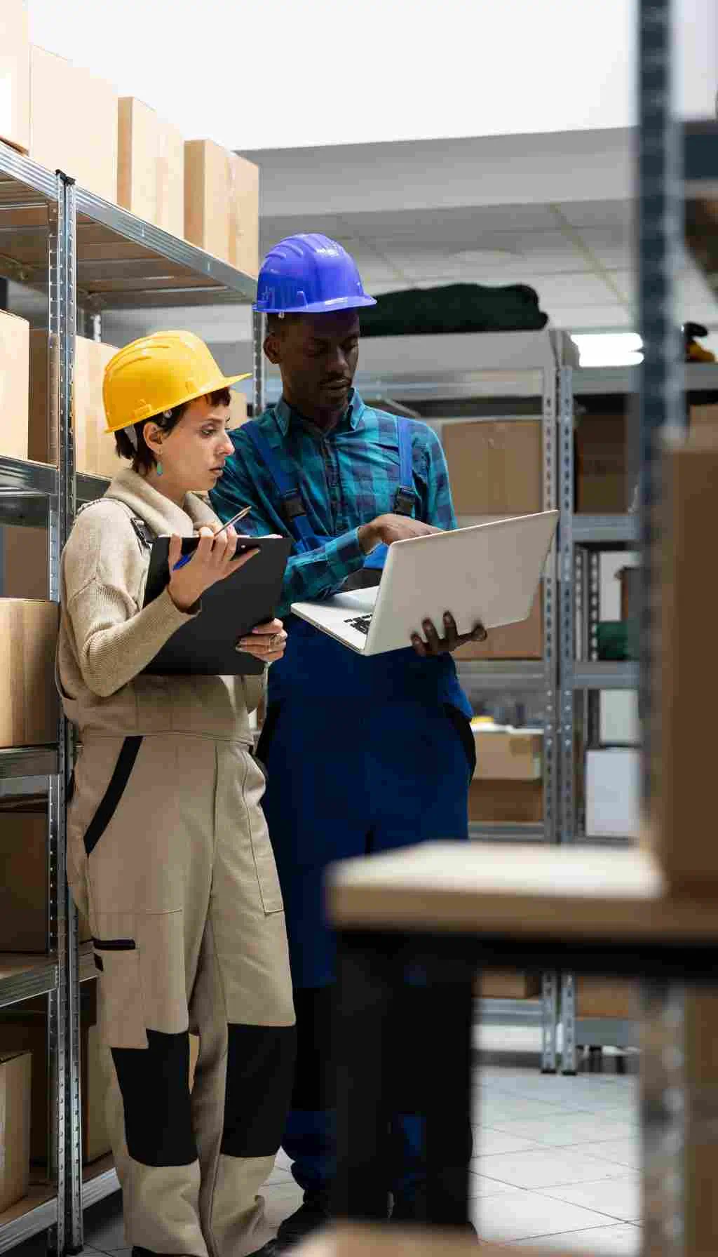 Two workers wearing safety helmets reviewing data in a warehouse, highlighting workplace safety and social sustainability