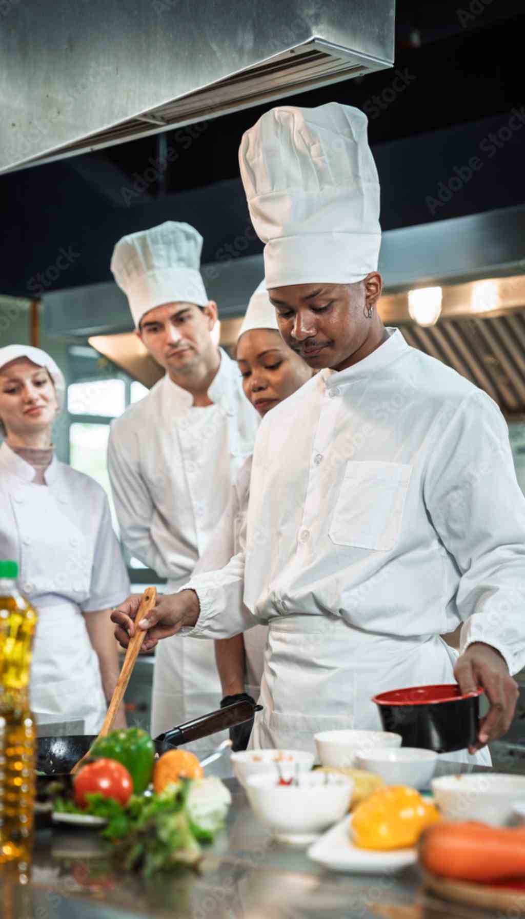 Chef demonstrating a cooking technique to a diverse team of kitchen staff in a professional restaurant, highlighting visual learning and non-verbal food safety training.