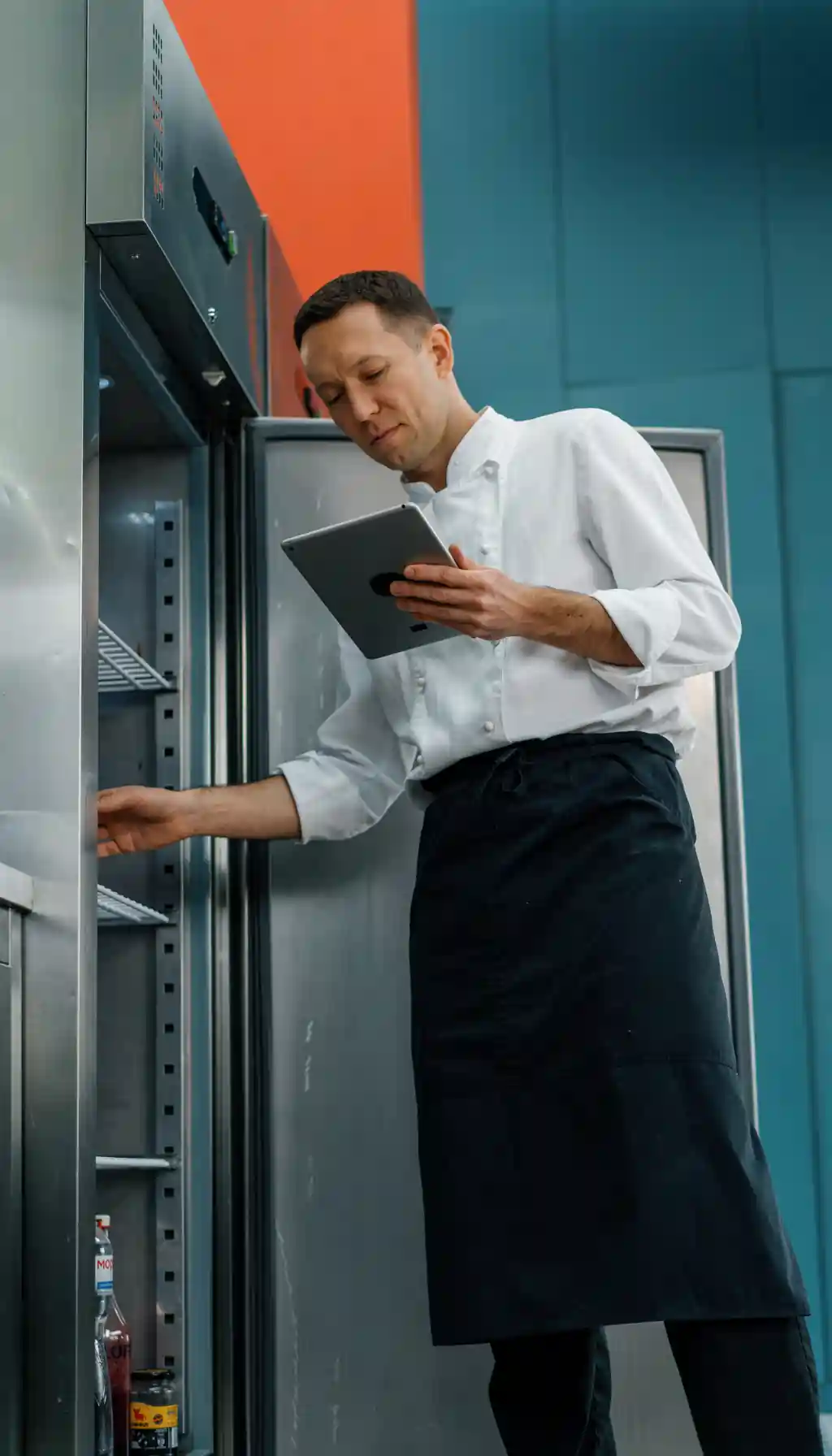 Hotel kitchen staff member using a tablet to check refrigerator temperature and compliance records