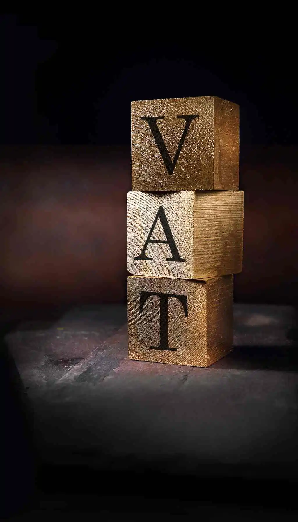 Wooden Blocks Stacked to Represent VAT Stacked wooden blocks displaying the letters V, A, and T against a dark background.