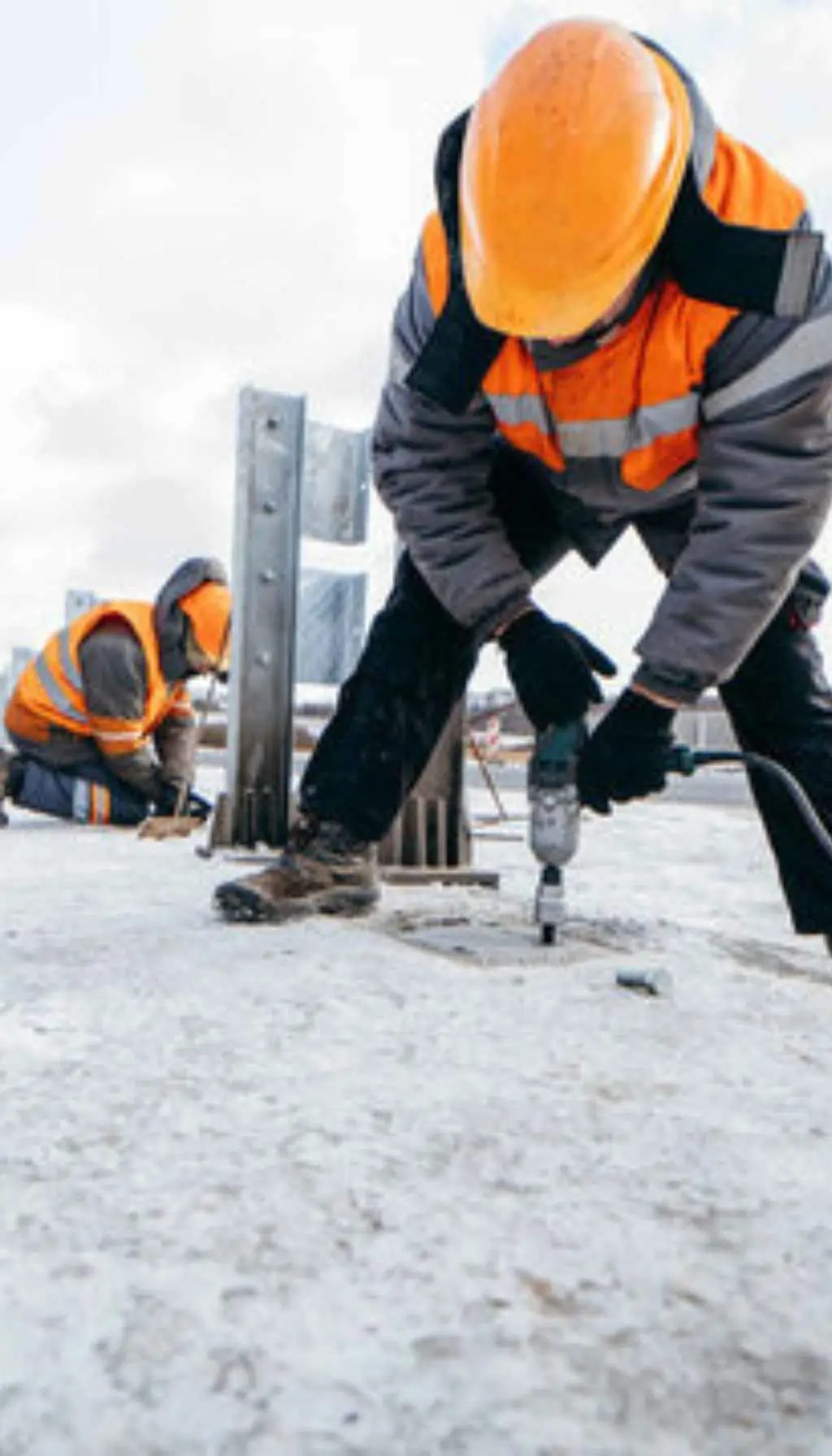 Construction workers drilling and working outdoors on a snowy site wearing safety helmets and high-visibility jackets