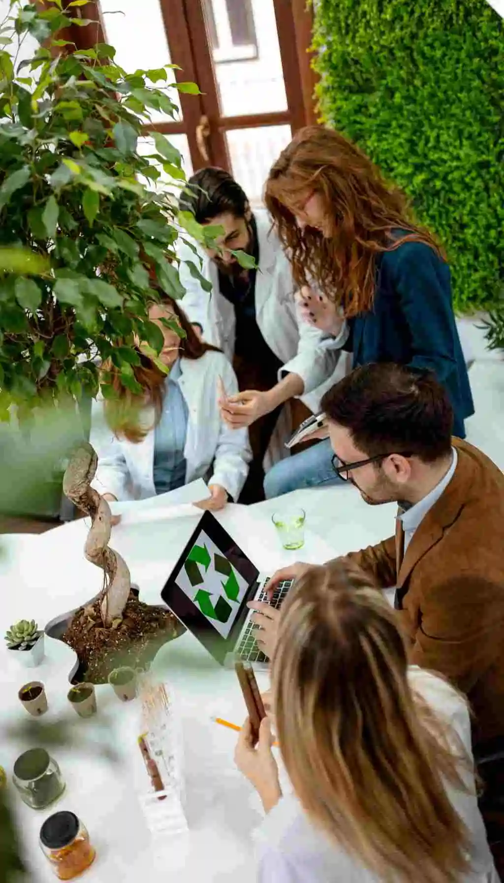 Team of professionals discussing sustainability strategy with eco-friendly visuals on a laptop, representing ESG integration and social responsibility in business.