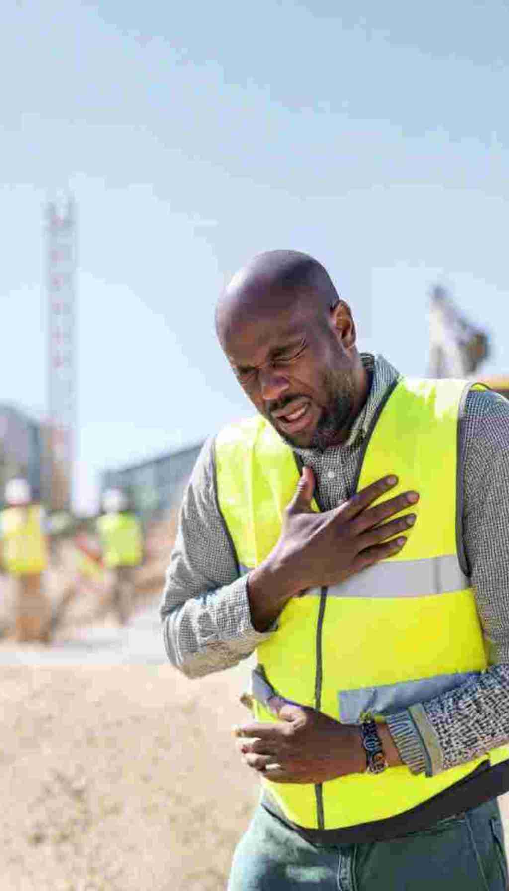 Cardiovascular Health and Safety: Recognising the Warning Signs at Work A construction worker wearing a high-visibility vest clutching his chest on-site, illustrating the importance of recognising cardiovascular health risks in the workplace.