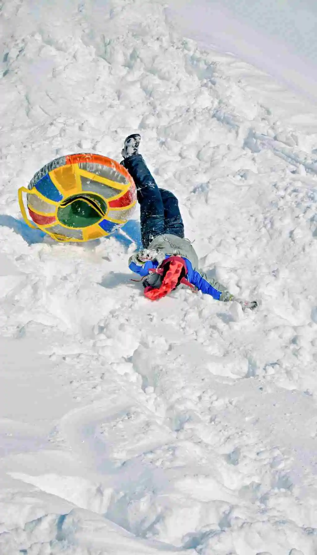 Person lying in deep snow after falling from an inflatable snow tube, showing the risks of slips and falls in icy winter conditions.