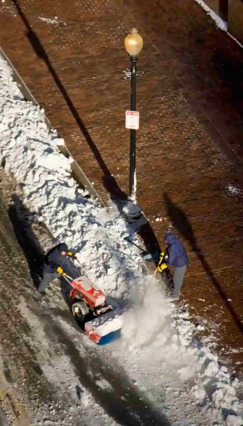 Two rescue workers in red jackets digging in deep snow during a winter emergency operation in a forest.