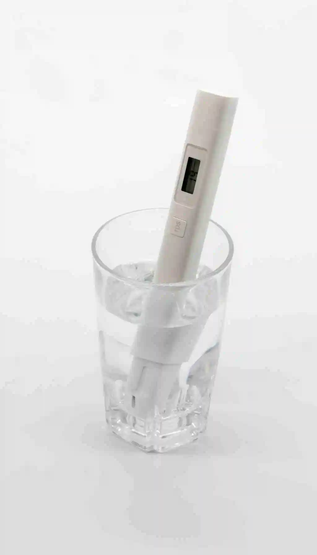 A digital pH meter resting in a glass of clear liquid during calibration, shown against a clean white background.