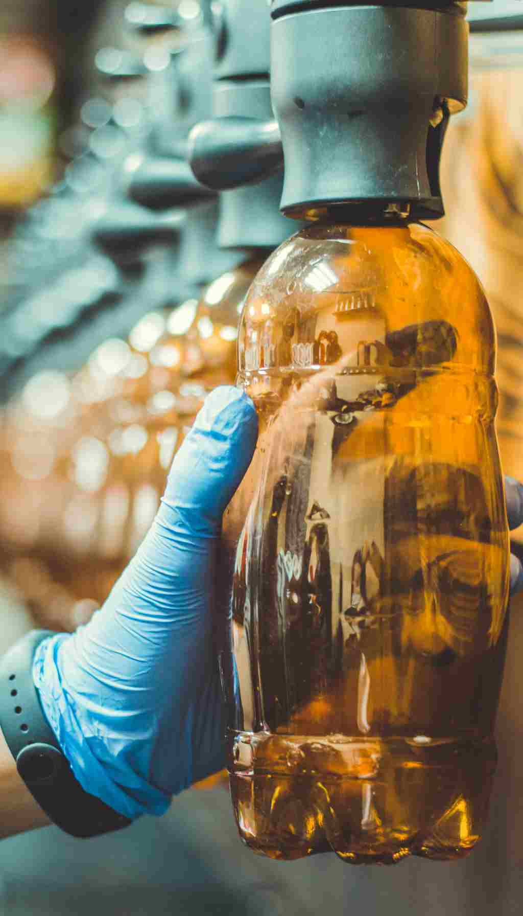 Gloved Worker Filling Plastic Beverage Bottle in Production Line A worker wearing a blue glove holds a plastic bottle being filled on a beverage production line, highlighting hygiene and food safety procedures.