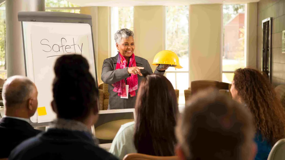 Workplace Safety Training Session Promoting a Positive Safety Culture Trainer holding a yellow safety helmet while delivering a workplace safety presentation to employees during a training session.