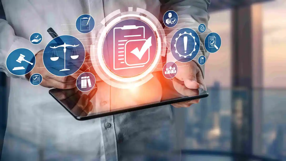 Digital Compliance and HSEQ Management Technology Digital compliance interface showing safety, quality, and regulatory icons above a tablet held by a person, symbolising modern HSEQ management tools and digital safety systems.
