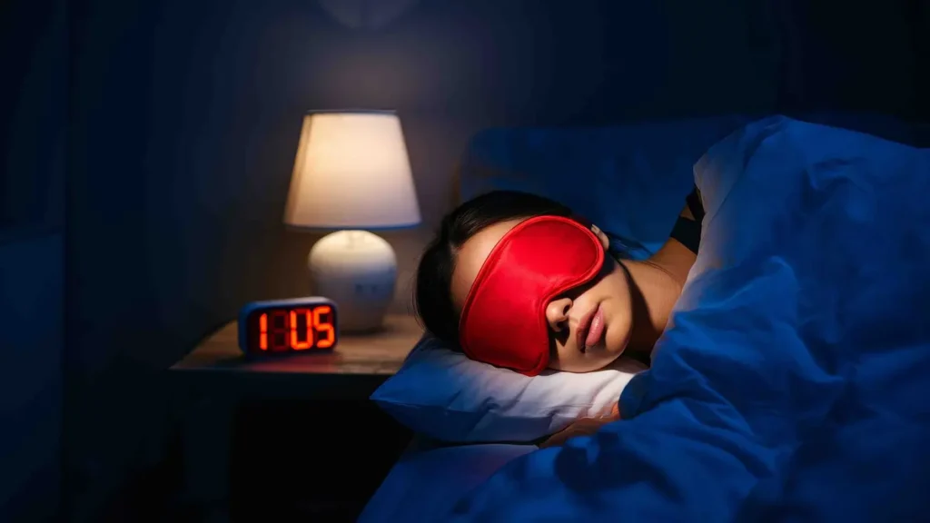 Person sleeping with an eye mask beside a digital alarm clock showing late night time