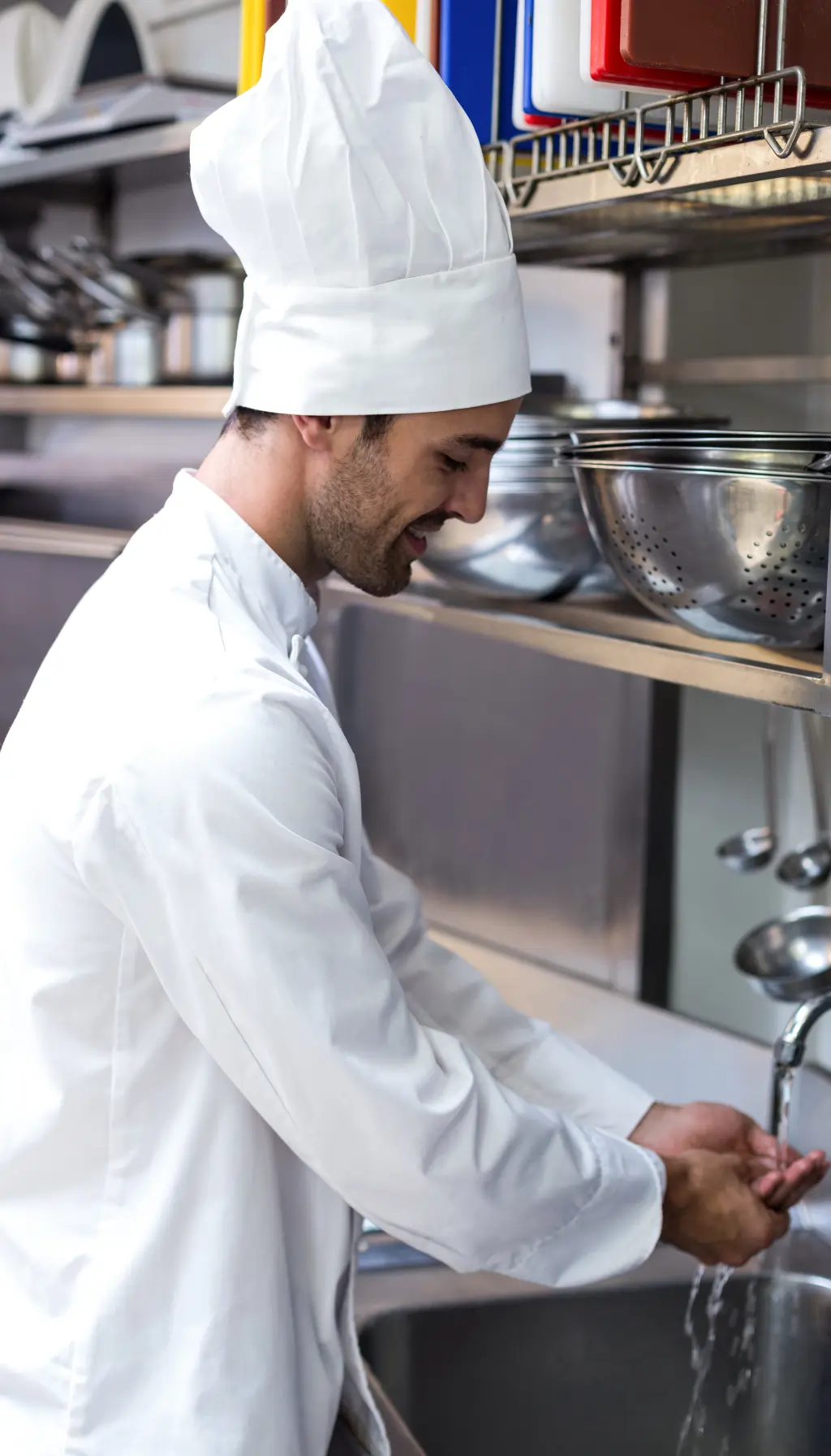 Chef washing hands at a stainless steel sink in a professional kitchen, demonstrating correct personal hygiene and food safety practices.