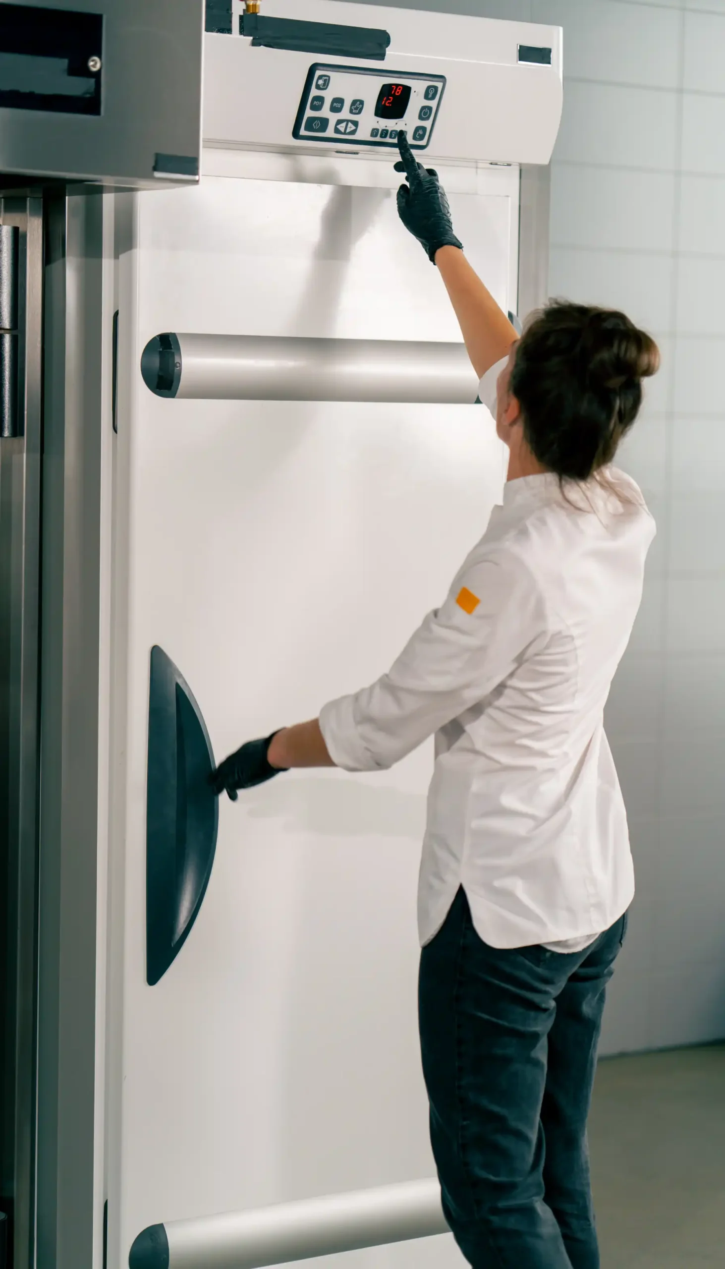 Food handler adjusting a commercial refrigeration unit temperature control in a professional food storage area.