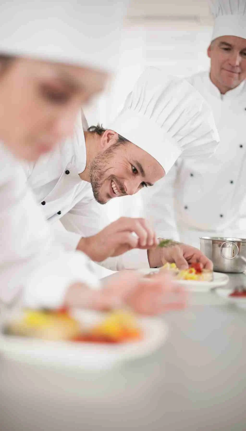 Chefs in a professional commercial kitchen carefully plating food while following hygiene and food safety procedures.