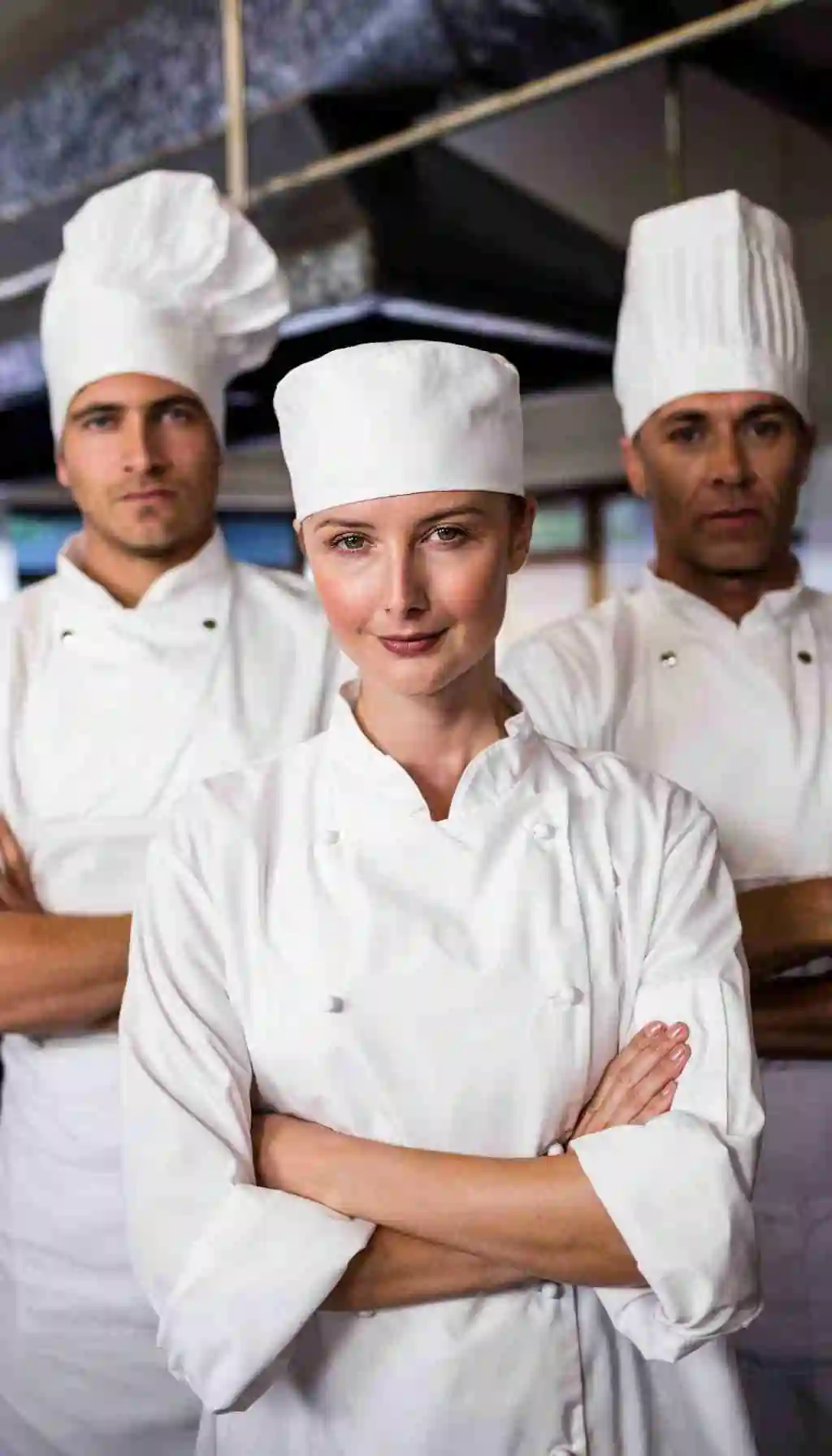 Head chef and senior kitchen staff wearing white chef uniforms and hats standing confidently in a commercial kitchen