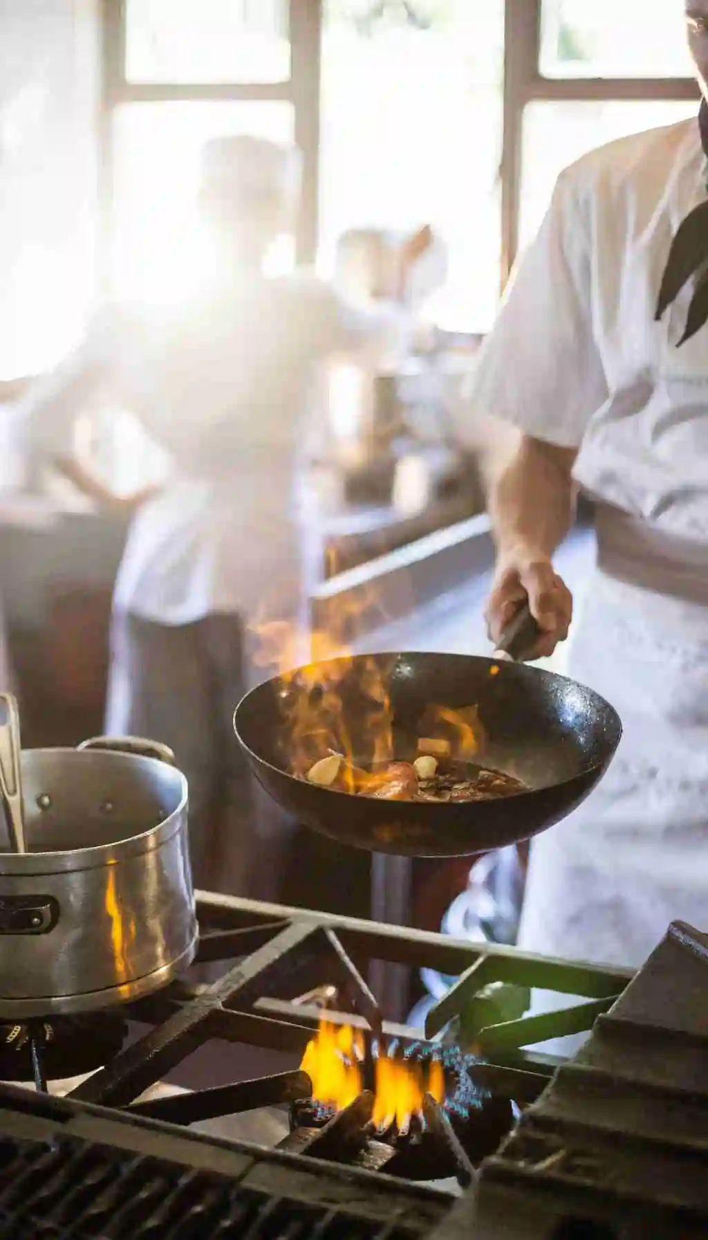 Chef cooking food in a frying pan over an open gas flame in a professional commercial kitchen