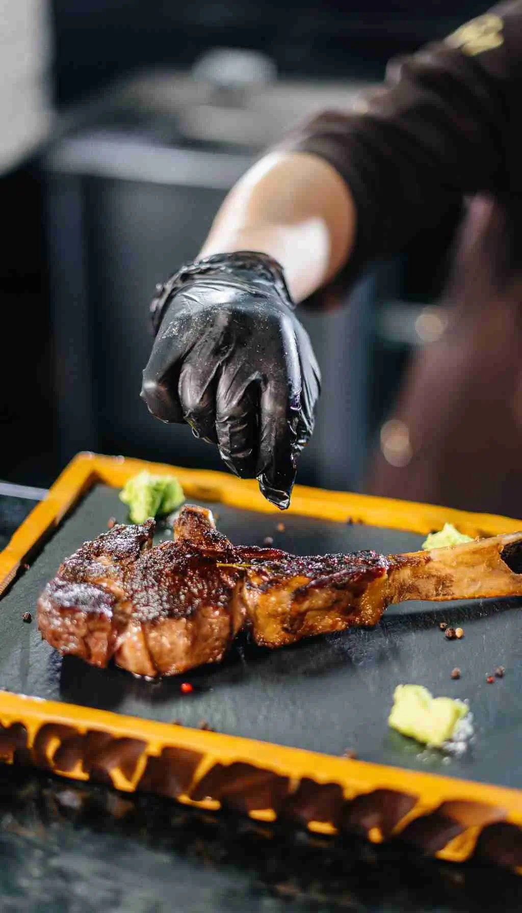 Chef wearing protective gloves plating cooked steak in a hygienic commercial kitchen