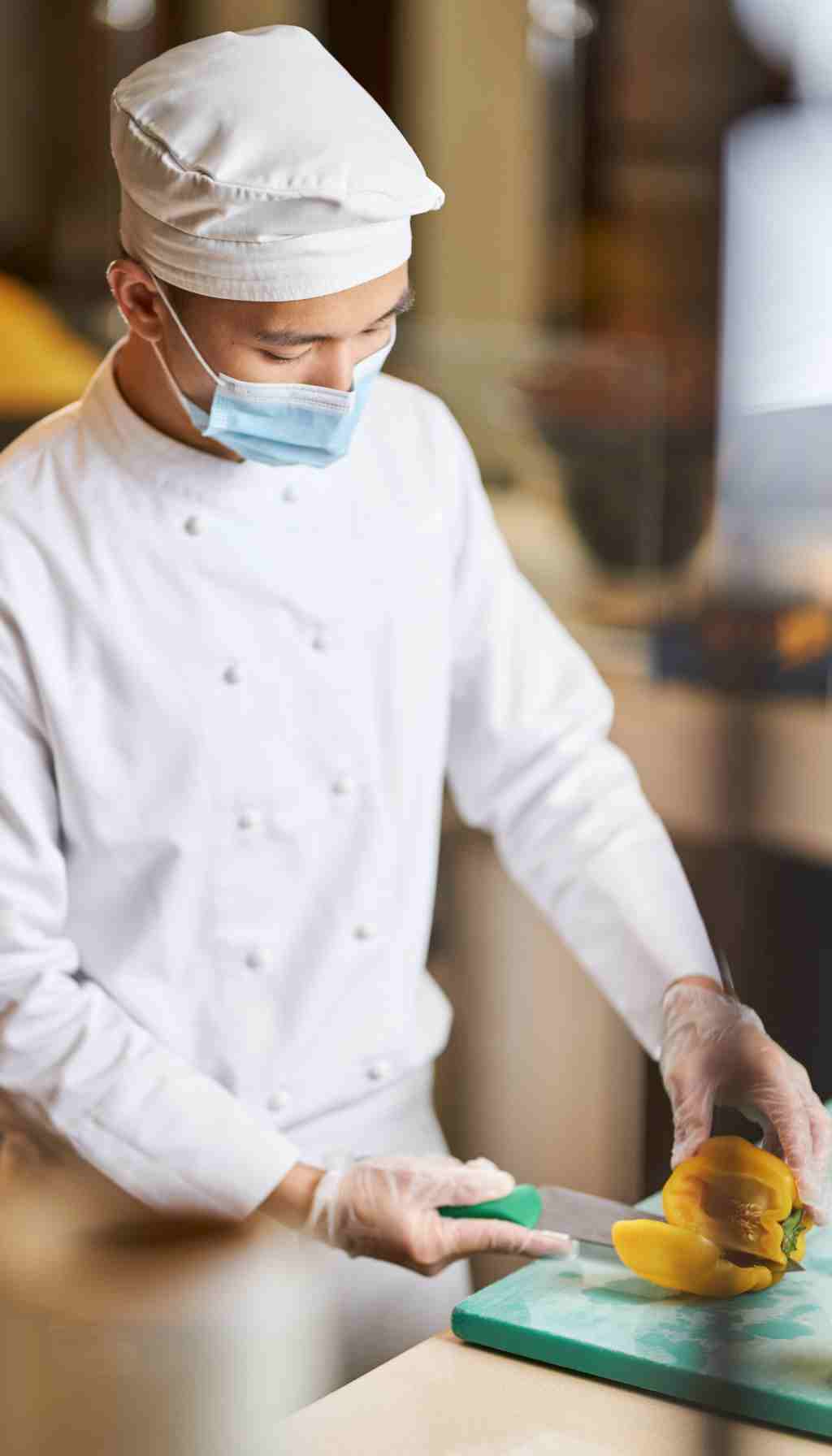 Food Hygiene Practices in Professional Food Preparation Food handler wearing protective clothing and gloves preparing fresh vegetables in a hygienic kitchen