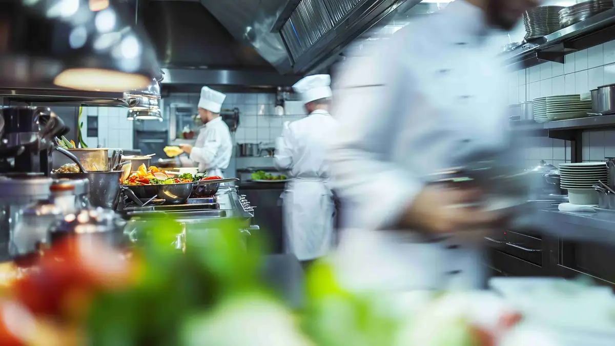 Chef bending forward to lift a food container from a low shelf in a commercial kitchen