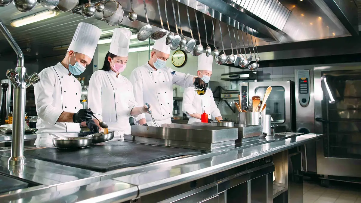 Food handler wearing gloves preparing fresh vegetables at a refrigerated prep station