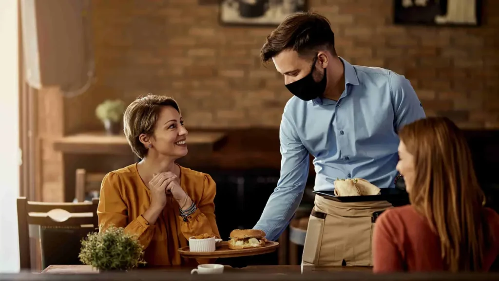 Waiter wearing face mask serving food to restaurant customers at table
