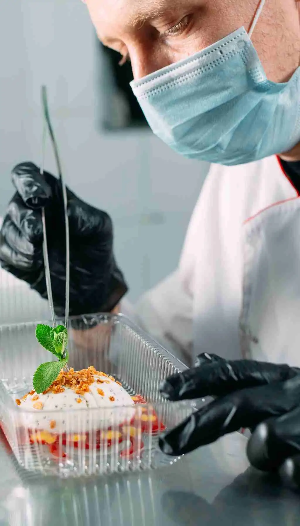 Healthcare catering staff plating meals while a supervisor checks standards using a clipboard