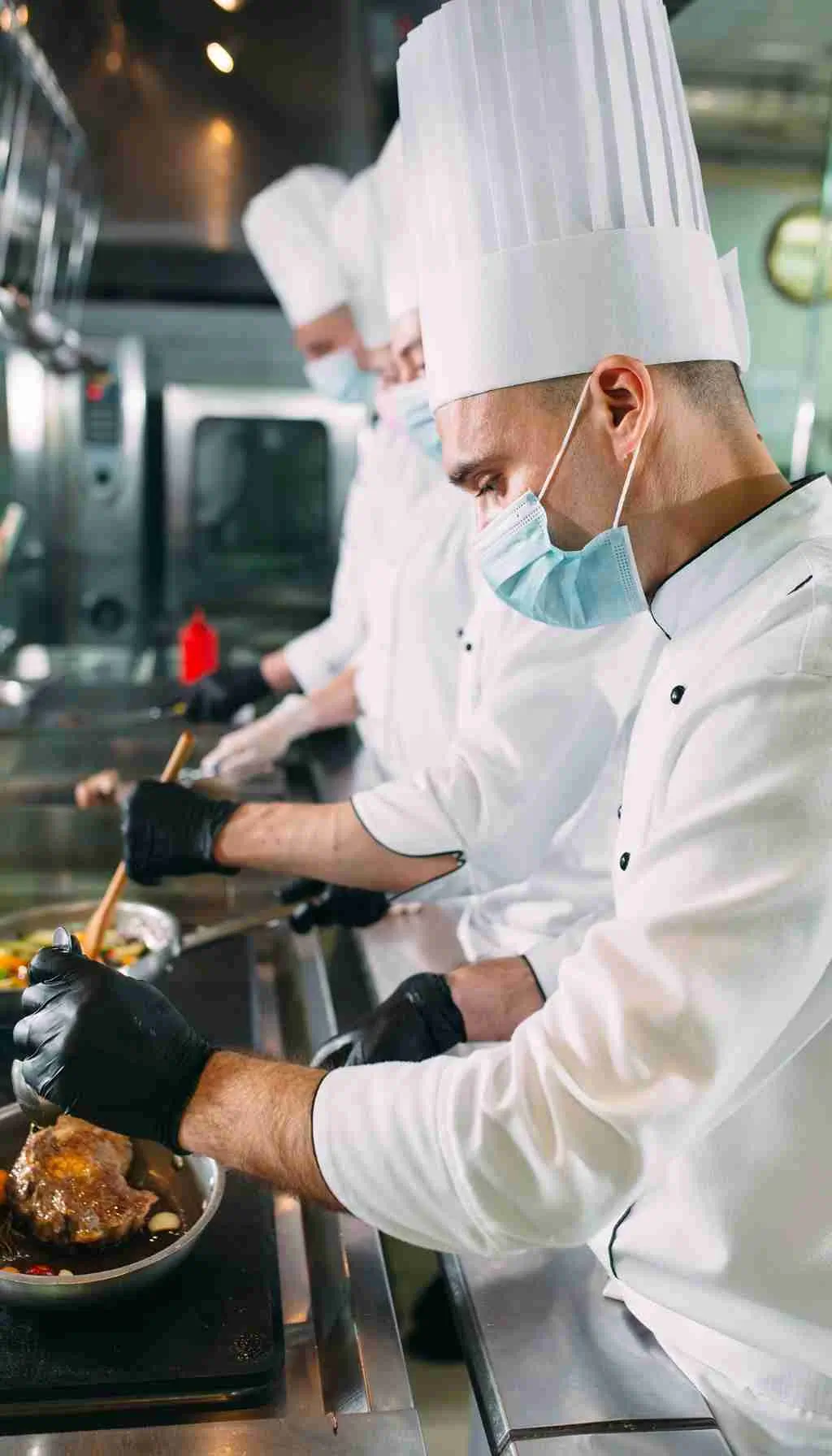 Healthcare catering staff plating meals while a supervisor checks standards using a clipboard